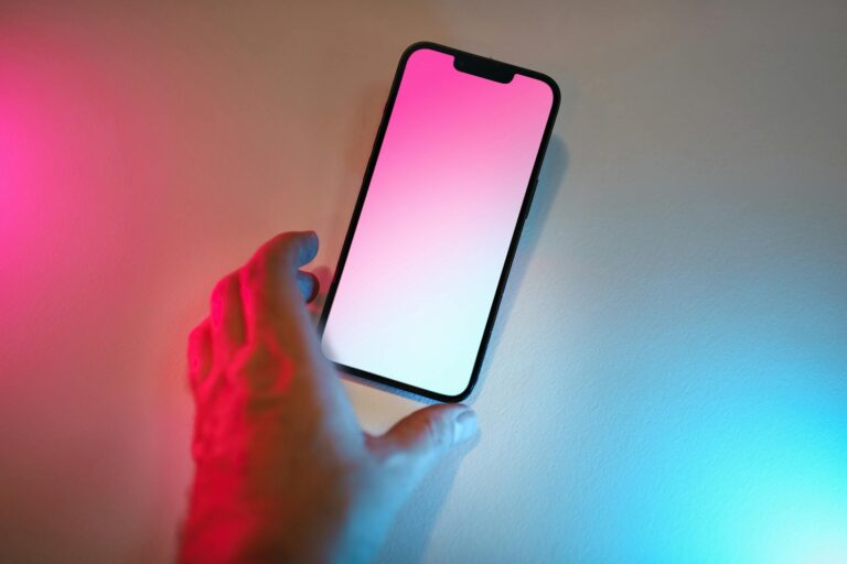 A hand reaches for a smartphone with a colorful gradient screen and ambient lighting.