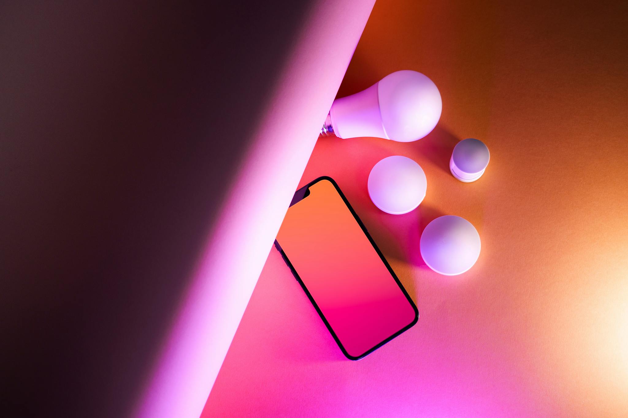 Vibrant artistic composition of smart home bulbs and smartphone on a gradient background.